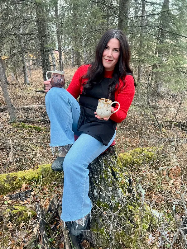 The owner sitting in a forest showing one of her handmade ceramic products