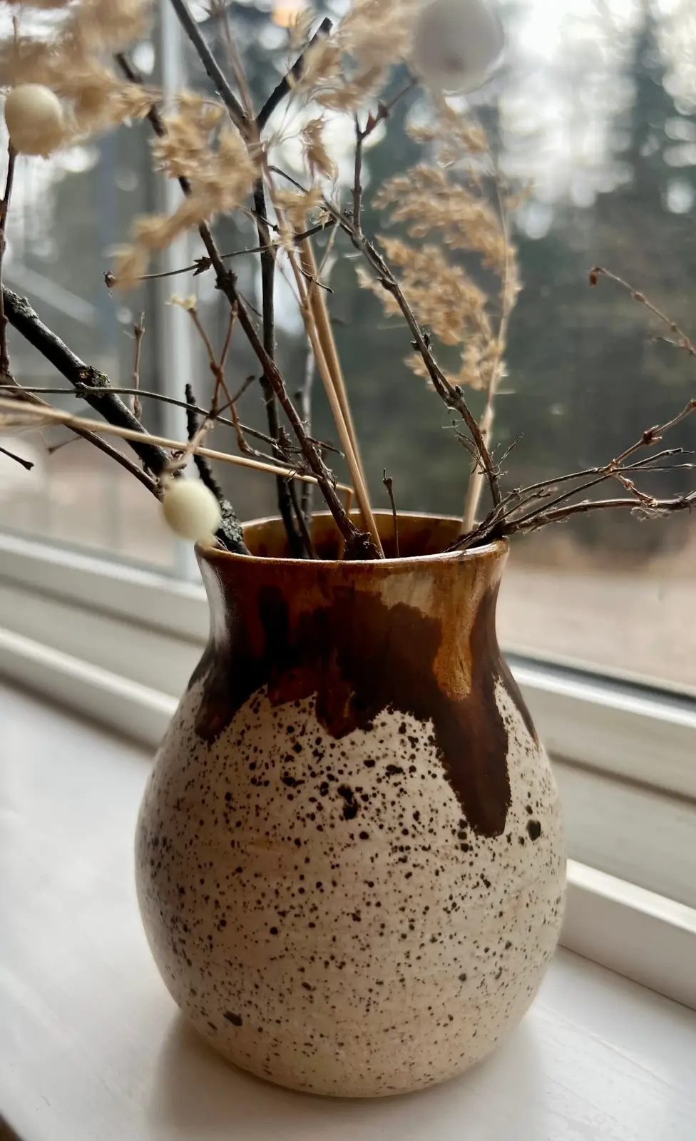 A brown and white, handmade vase with plants.
