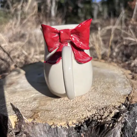 Wheel thrown cup featuring a red sculpted bow.