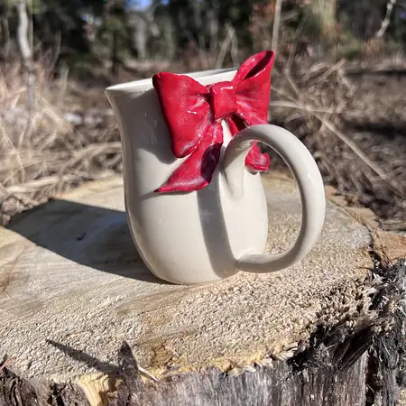 Wheel thrown cup featuring a red sculpted bow.