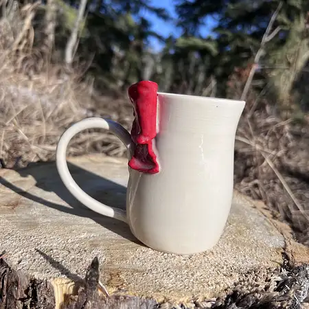 Wheel thrown cup featuring a red sculpted bow.