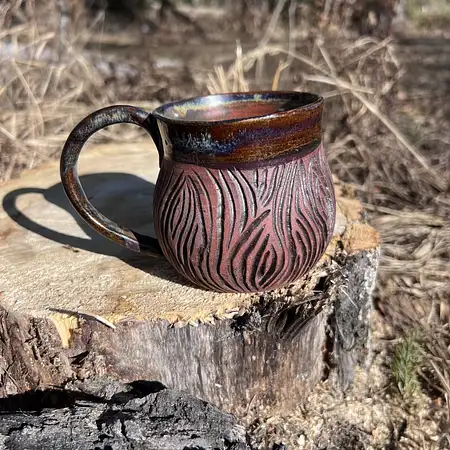 Dark clay thrown and carved in a tree bark pattern leaving the raw clay exposed. Interior and rim is glazed in a rusty dark glaze.
