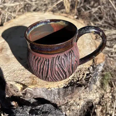Dark clay thrown and carved in a tree bark pattern leaving the raw clay exposed. Interior and rim is glazed in a rusty dark glaze.