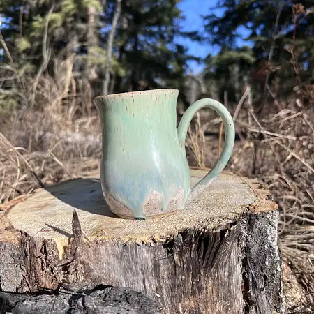 Speckled clay cup featuring a green and blue drippy glaze. 