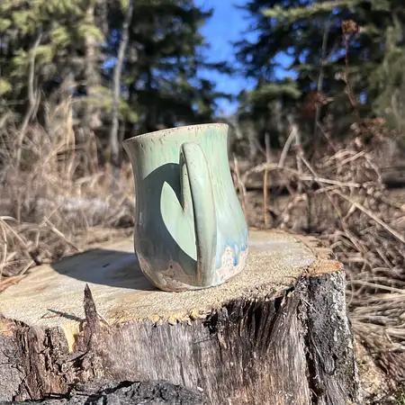 Speckled clay cup featuring a green and blue drippy glaze. 