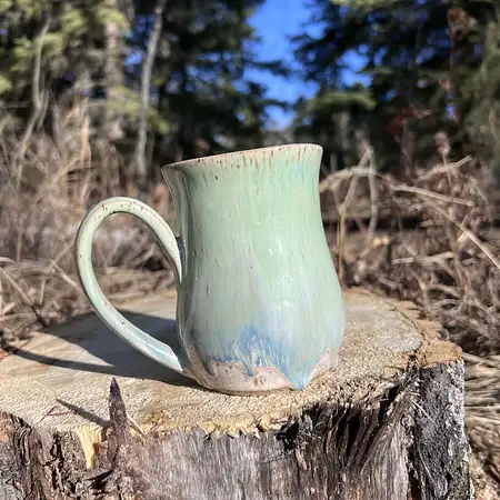 Speckled clay cup featuring a green and blue drippy glaze. 