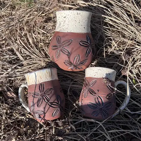 Dark brown clay hand thrown and carved featuring flowers and a earthy cream glaze.