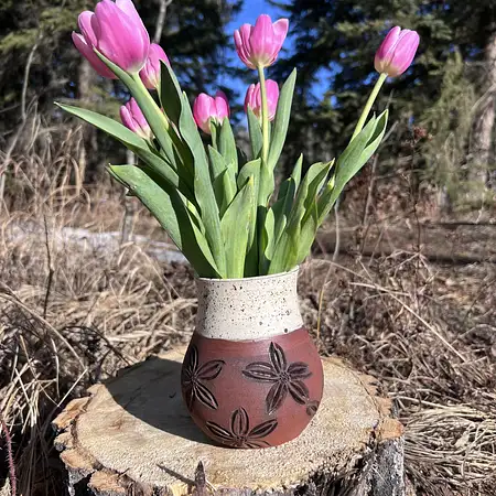 Dark brown clay hand thrown and carved featuring flowers and a earthy cream glaze.