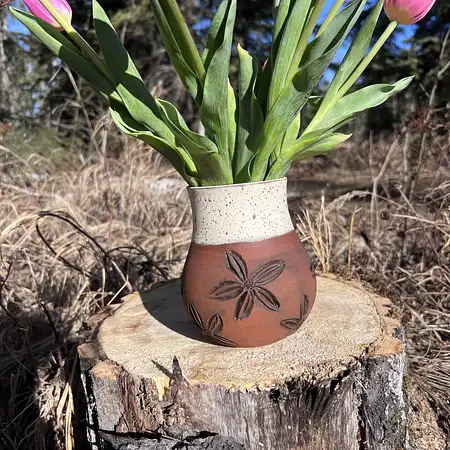 Dark brown clay hand thrown and carved featuring flowers and a earthy cream glaze.